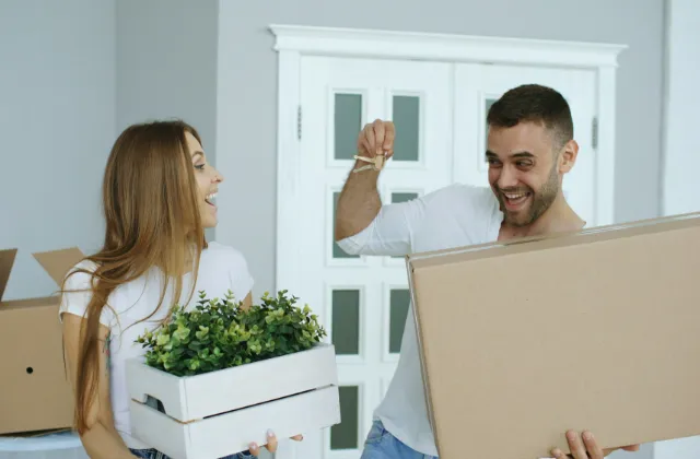 Couple carrying a moving box and a plant into their new home