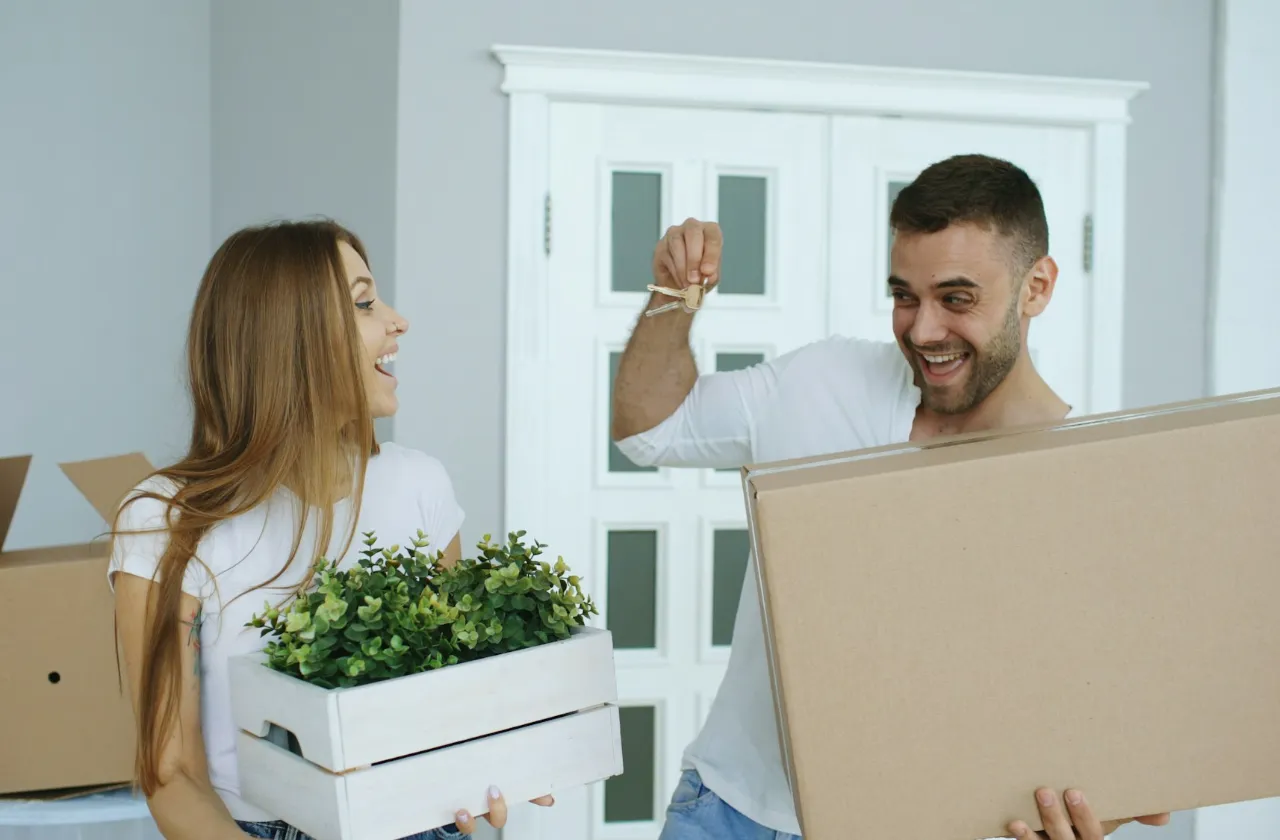 Couple carrying a moving box and a plant into their new home