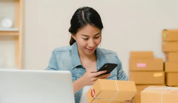 Store owner checking an order on her phone beside boxes and a laptop